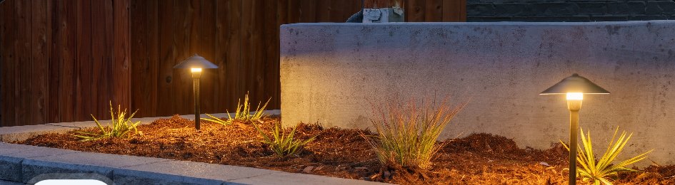 Lit retaining wall with mulch beds and landscape lighting at dusk